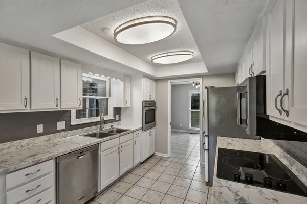 a large kitchen with a stove a sink dishwasher and a refrigerator with white cabinets