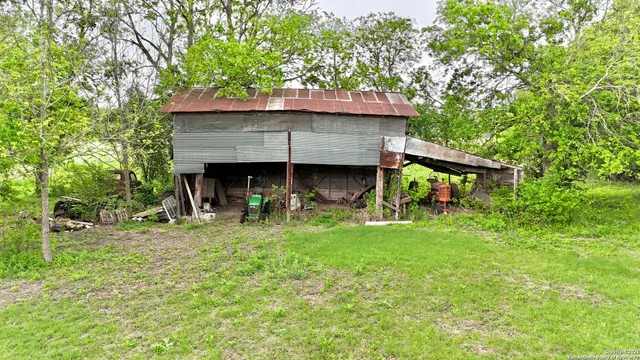 a view of a wooden house with a small yard and large trees