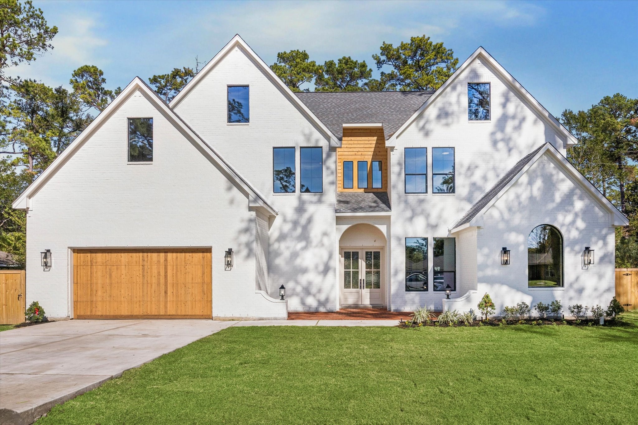  Modern alabaster exterior with large windows, wood accents, and a wide driveway leading to a three-car garage.
