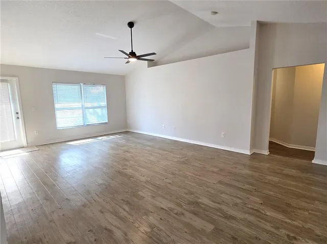 an empty room with wooden floor ceiling fan and windows
