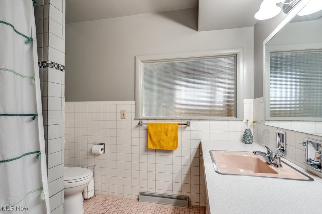 396 Sandhurst Road Akron, OH 44333 - Photo 33 of 50 Bathroom featuring a baseboard heating unit, vanity, tile walls, a shower with shower curtain, and a wainscoted wall