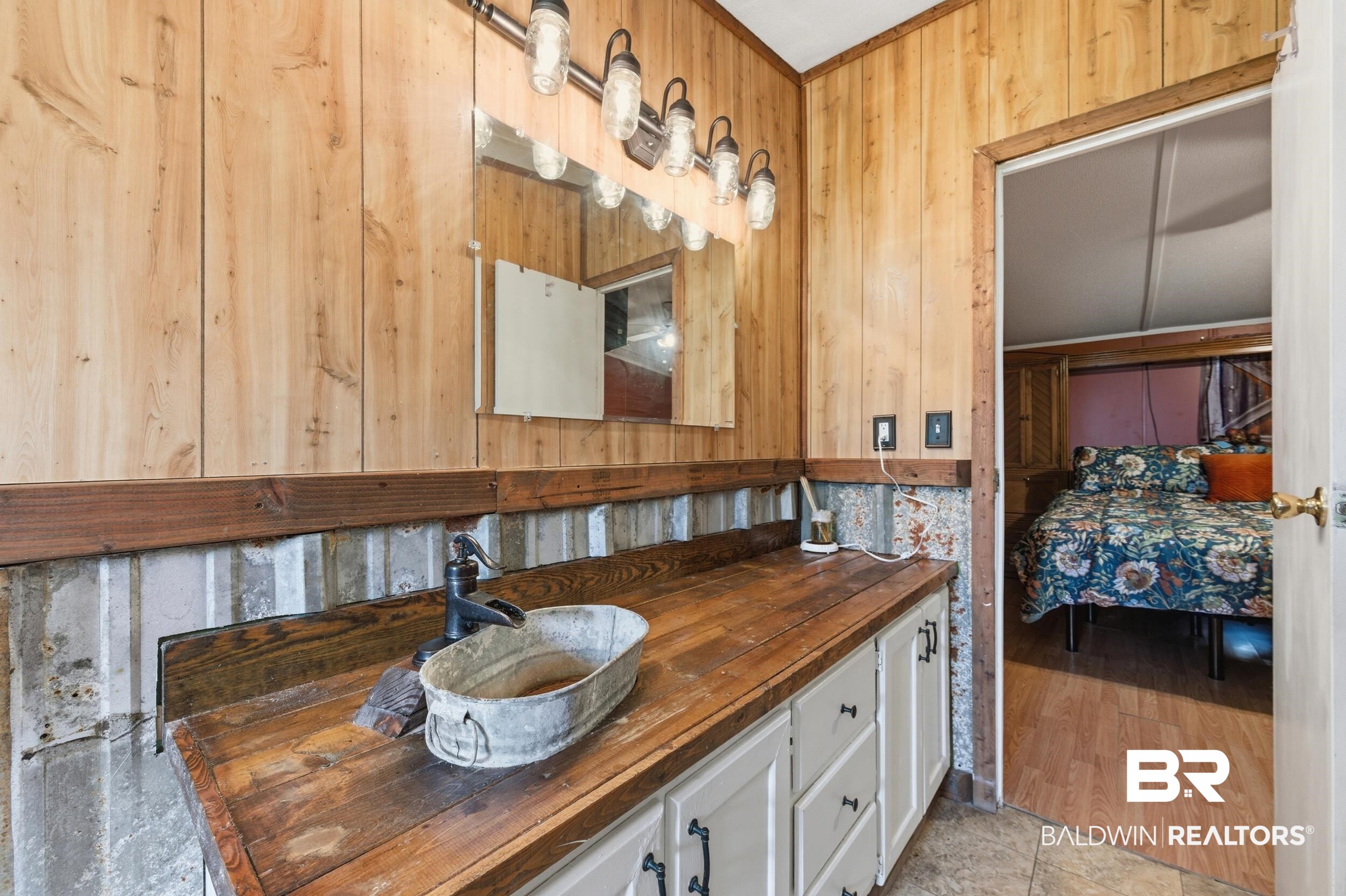 926 Tumbling Lane Atmore, AL 36502 - Photo 33 of 56 Wood-paneled bathroom featuring a rustic wood-finish countertop, white cabinetry with dark hardware, and a unique vessel sink