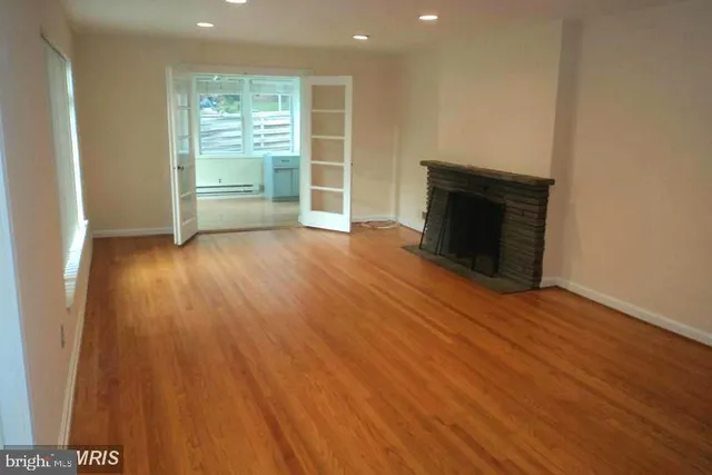 an empty room with wooden floor fireplace and windows