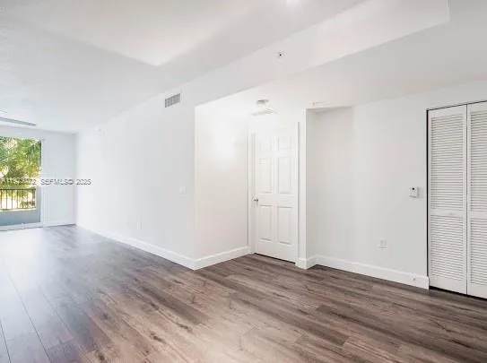 a view of an empty room with wooden floor and a ceiling fan