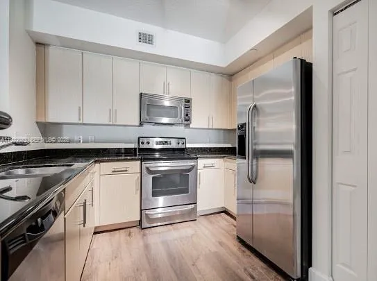 a kitchen with stainless steel appliances granite countertop a refrigerator a sink and white cabinets
