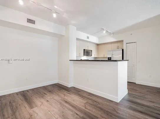 an empty room with wooden floor and kitchen