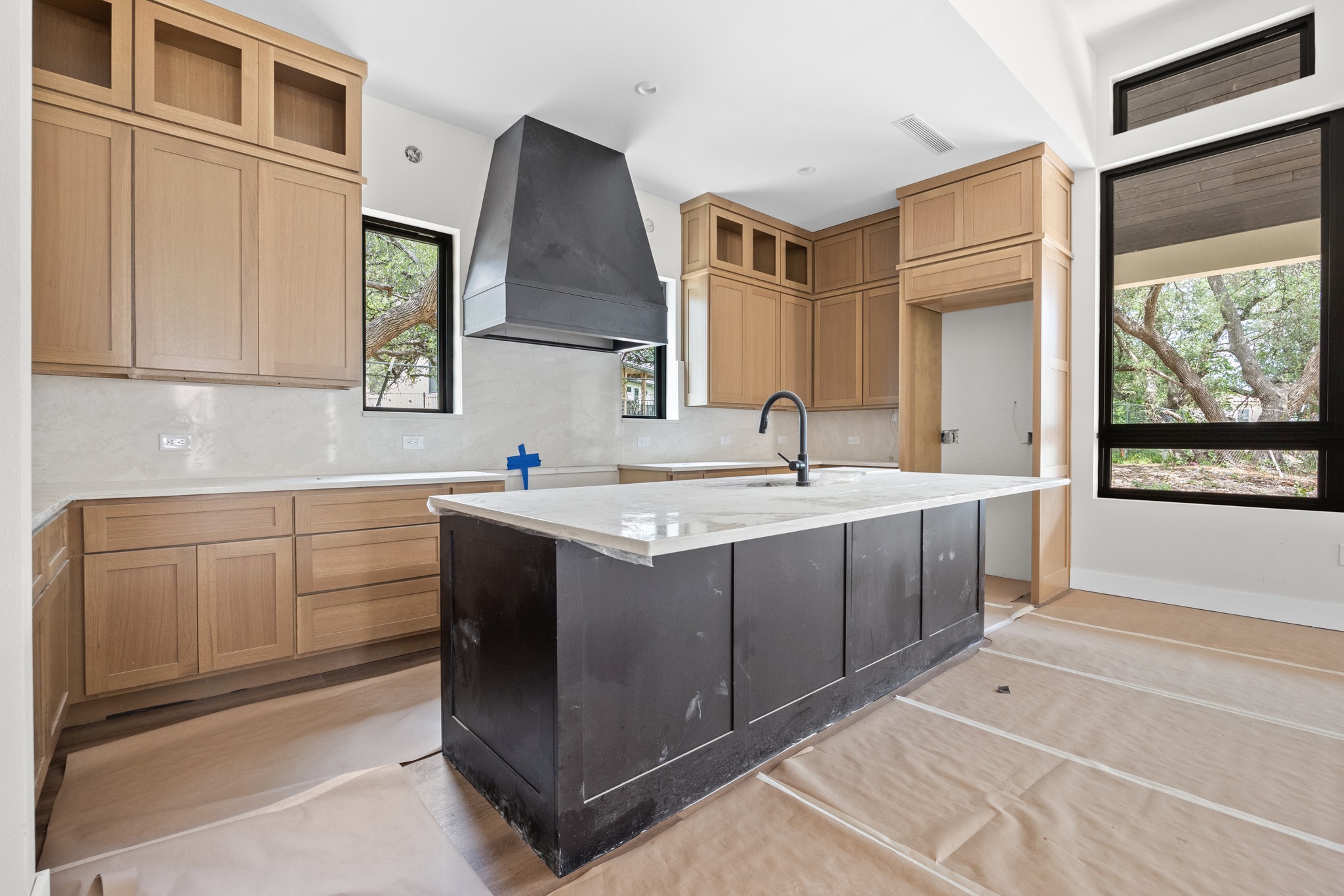 903 Flint Ridge Trail Georgetown, TX 78628 - Photo 9 of 39 Modern kitchen featuring a large central island with a contrasting dark base, light-toned cabinetry, a sleek black range hood, a white tile backsplash, and oversized windows