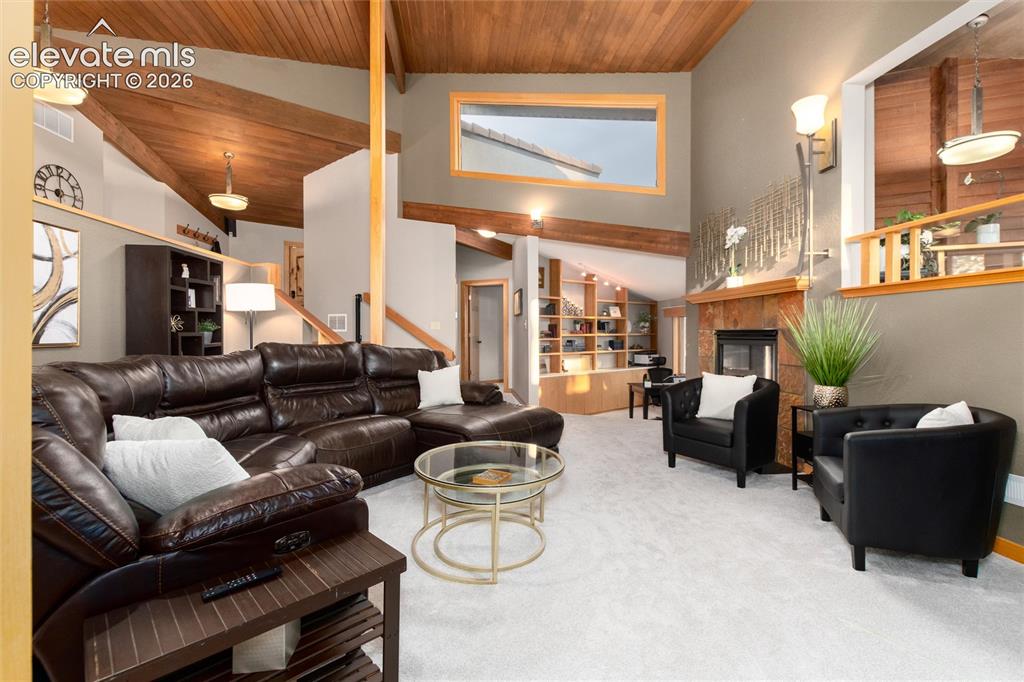 12730 Bridle Bit Road Colorado Springs, CO 80908 - Photo 15 of 50 Vaulted ceilings with exposed wood beams, light-toned carpeting, a stone fireplace, built-in shelving, and a large upper-level window
