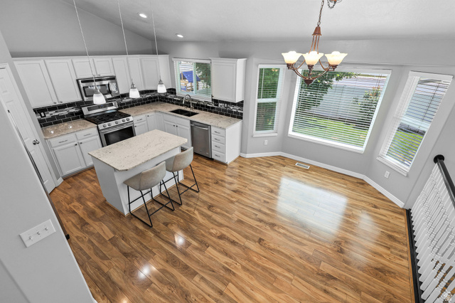 142 East 2675th Street South Clearfield, UT 84015 - Photo 13 of 49 Kitchen and dining area featuring wood-finish flooring, white cabinetry, dark subway tile backsplash, and light-toned countertops