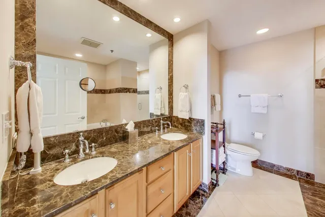 a bathroom with a granite countertop sink a toilet a mirror and a shower
