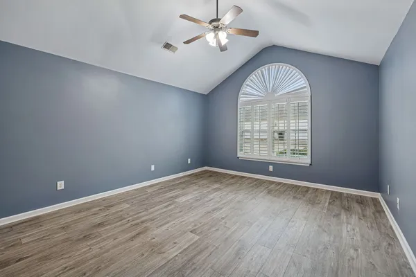 an empty room with wooden floor chandelier fan and windows