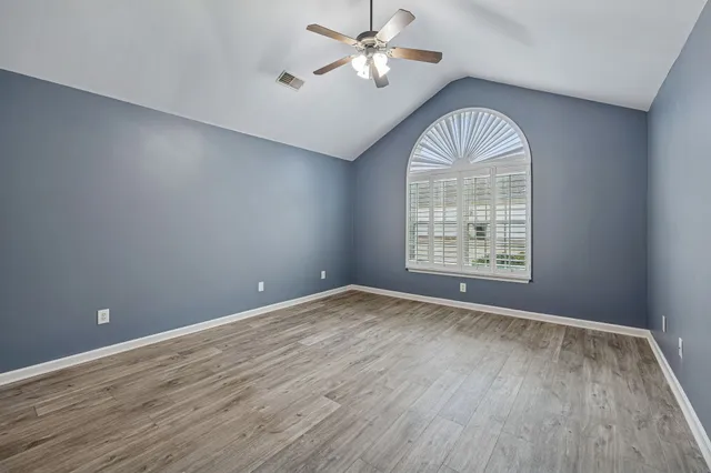 an empty room with wooden floor chandelier fan and windows