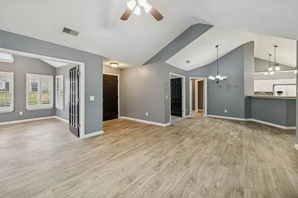 a view of an empty room with wooden floor and a kitchen