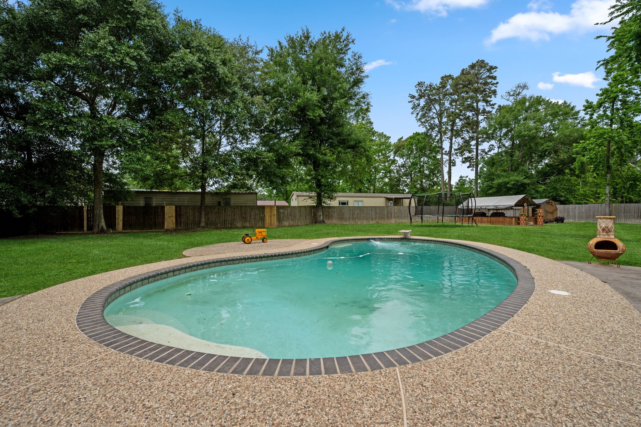 18 East Old Field Road Huffman, TX 77336 - Photo 25 of 35 The resort-style in-ground pool creates the ultimate private backyard retreat, surrounded by an expansive pebblestone patio. Towering mature trees in the backdrop provide a serene, secluded atmosphere perfect for relaxation or outdoor entertaining.