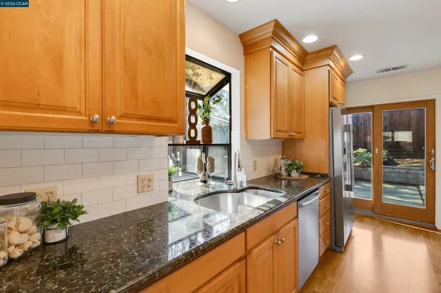 a kitchen with granite countertop a sink stainless steel appliances white cabinets and a window