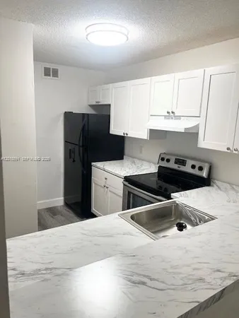 a kitchen with stainless steel appliances a refrigerator a sink a stove and white cabinets