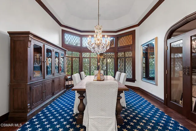 a dining room with wooden floor a chandelier a rug a fireplace and a chandelier
