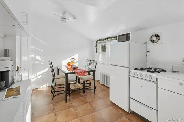 a white kitchen with a stove a refrigerator and a dining table with wooden floor