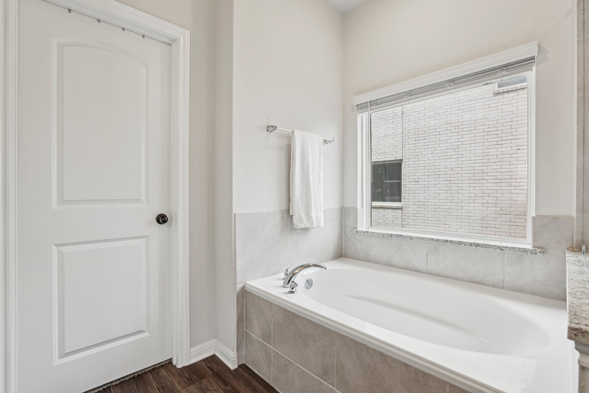 204 Swinging H Lane Georgetown, TX 78633 - Photo 15 of 39 Relaxing soaking tub with a tiled surround and a window overhead, complemented by a white paneled door and dark wood flooring