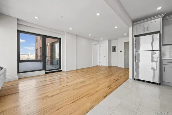 a view of an empty room with wooden floor and a kitchen