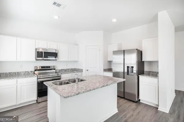 a kitchen with stainless steel appliances granite countertop a stove top oven a refrigerator and white cabinets with wooden floor