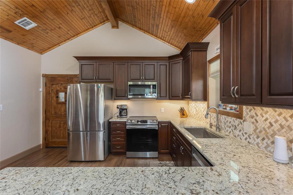 210 Spring Branch Trail North Springtown, TX 76082 - Photo 11 of 36 Kitchen featuring a vaulted wood-paneled ceiling, dark wood cabinetry, stainless steel appliances, light granite countertops, and a patterned tile backsplash