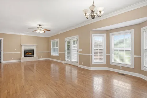 a view of an empty room with wooden floor and a ceiling fan