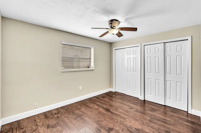 an empty room with wooden floor chandelier fan and windows