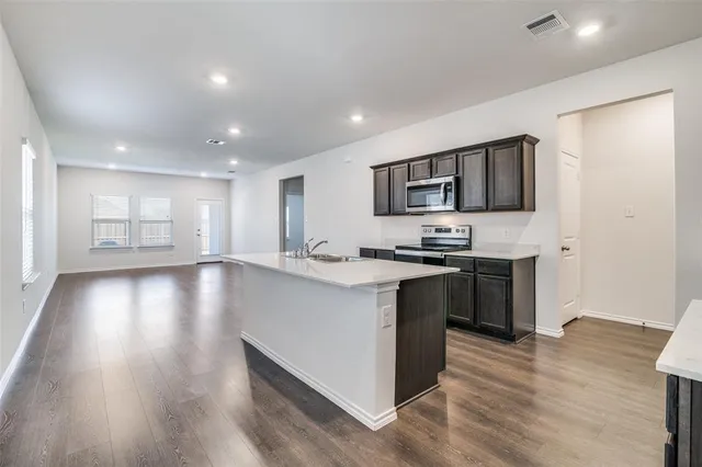 a kitchen with stainless steel appliances granite countertop a stove top oven a sink dishwasher a refrigerator and a microwave with wooden floor
