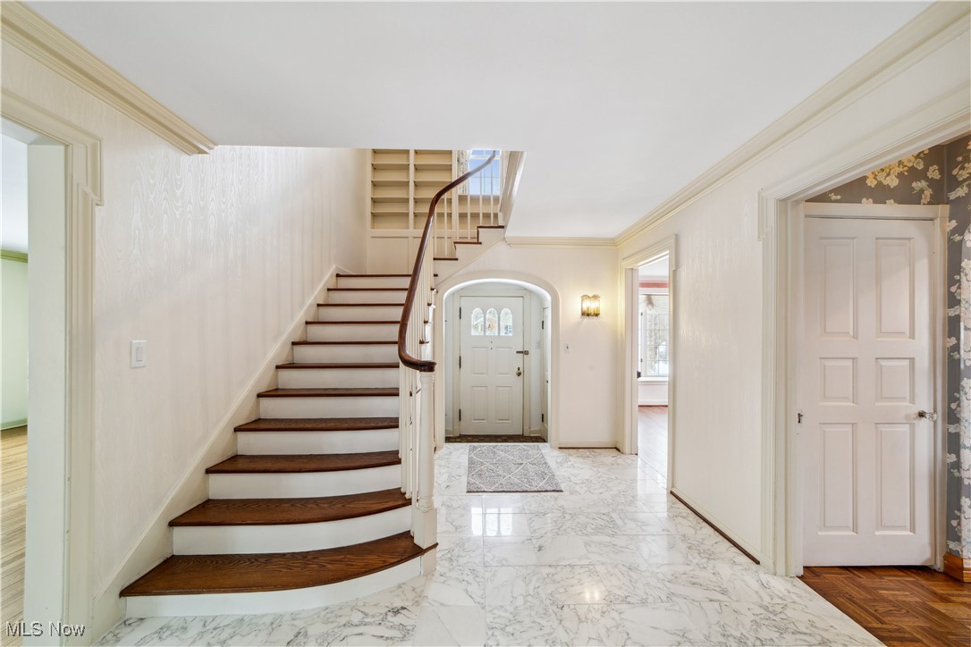 Entrance foyer with arched walkways, baseboards, marble finish floor, stairway, and crown molding