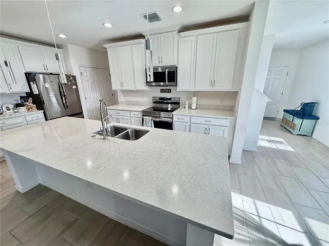 a kitchen with stainless steel appliances a stove a sink a microwave a refrigerator and white cabinets