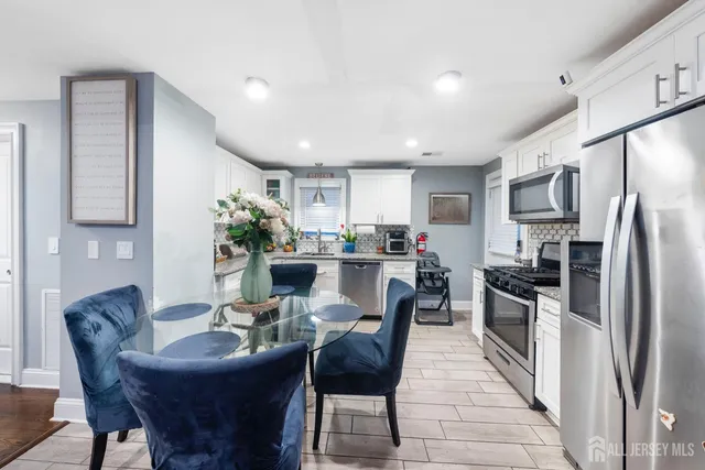 a kitchen with stainless steel appliances granite countertop a dining table chairs refrigerator and sink