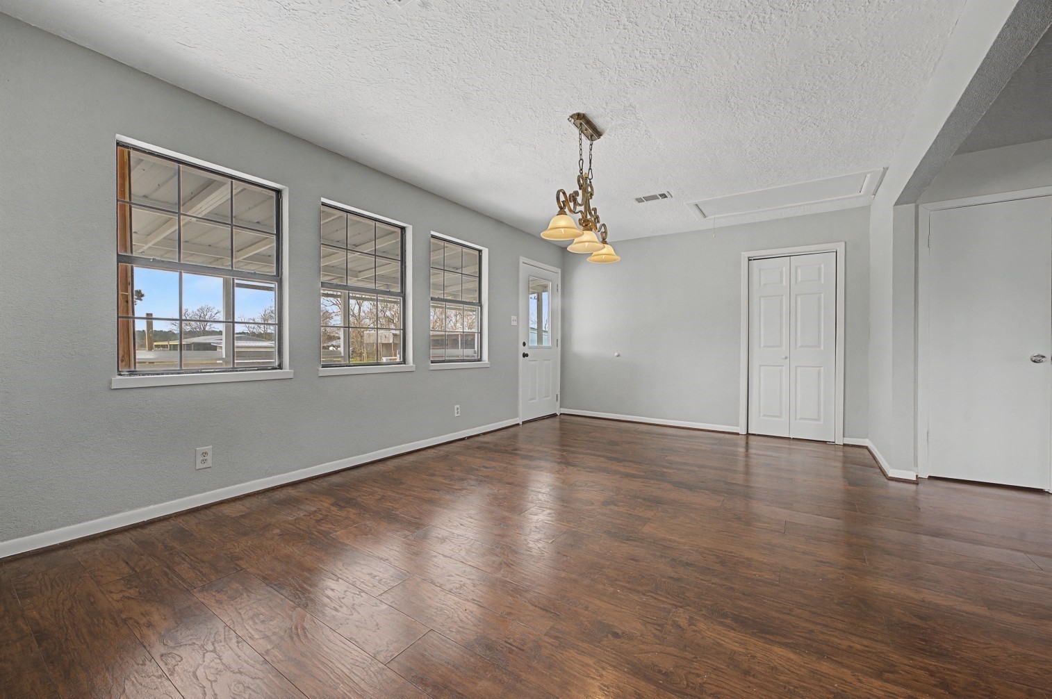 14077 Hamshire Road Hamshire, TX 77622 - Photo 12 of 39 This room features ample natural light from three large windows, and a classic chandelier. It includes a white door leading outside and a closet for storage, making it a versatile space for dining or living.