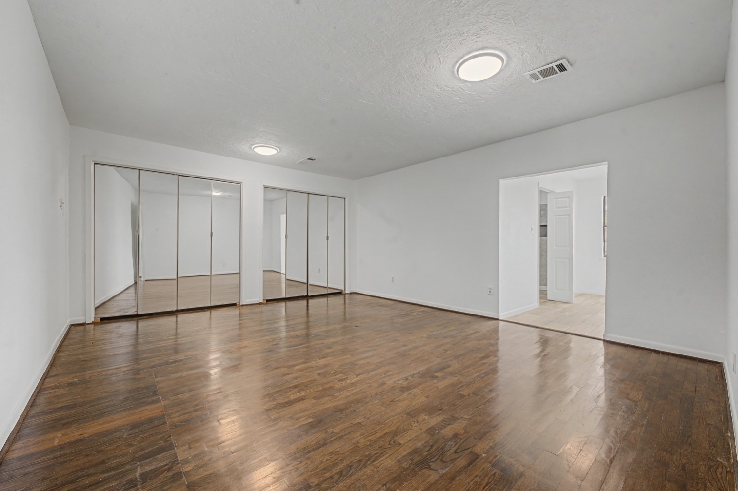 14077 Hamshire Road Hamshire, TX 77622 - Photo 17 of 39 This spacious primary room features sleek beautiful floors, mirrored closet doors for a modern touch, and bright overhead lighting. The neutral walls create a versatile backdrop, with an open doorway leading to spacious bathroom.