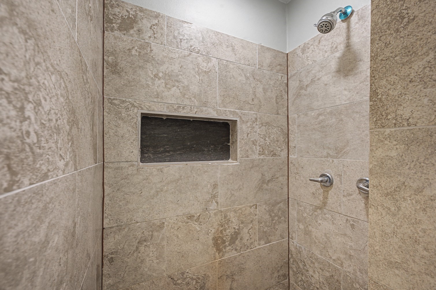 14077 Hamshire Road Hamshire, TX 77622 - Photo 20 of 39 This photo shows a modern shower with beige stone tiles, a built-in wall niche for storage, and a sleek showerhead and controls.