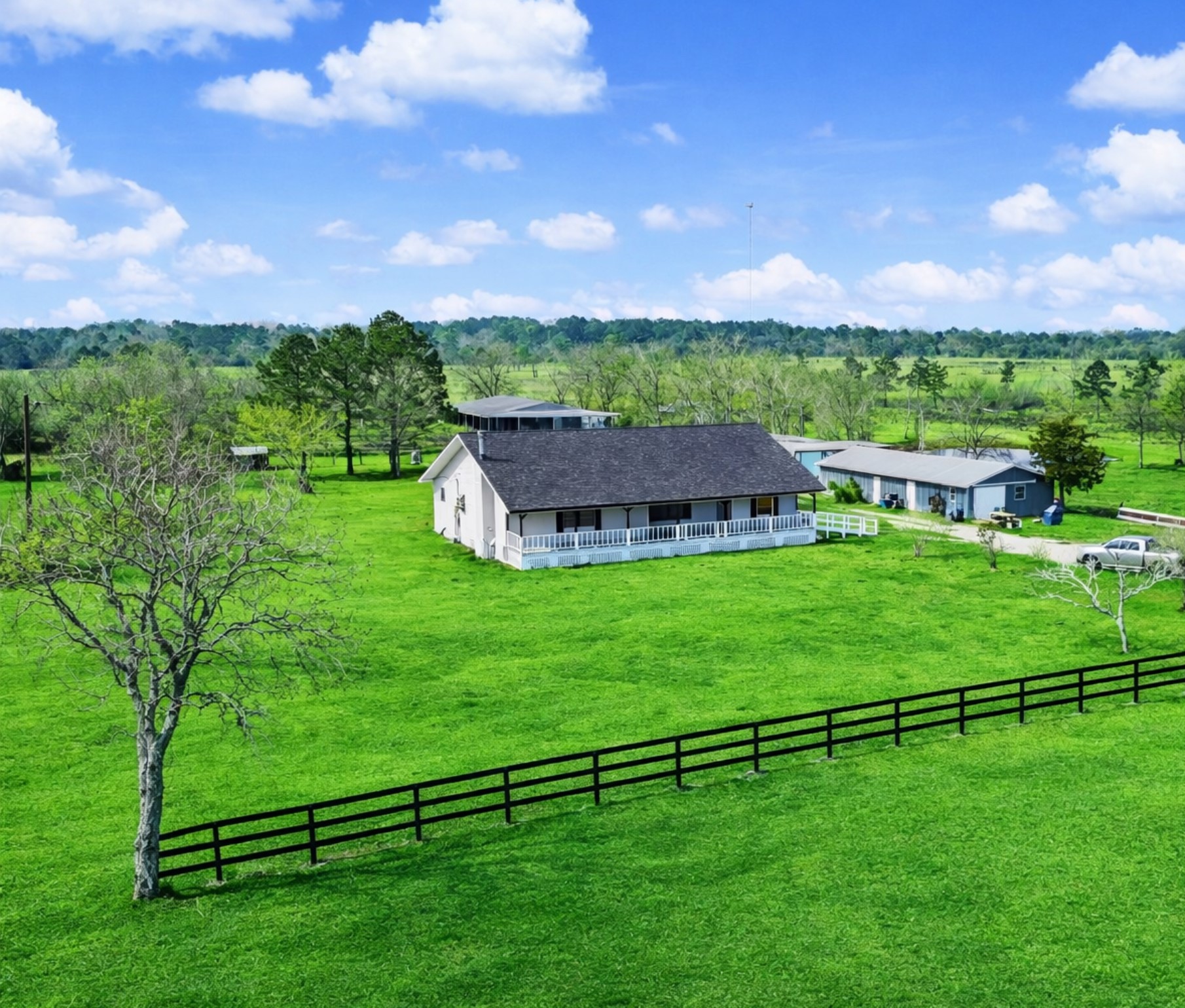 14077 Hamshire Road Hamshire, TX 77622 - Photo 2 of 39 This photo showcases a charming country home set amidst expansive green fields. The property includes a large house with a wraparound porch, additional outbuildings, and a picturesque rural landscape, ideal for those seeking tranquility and space.