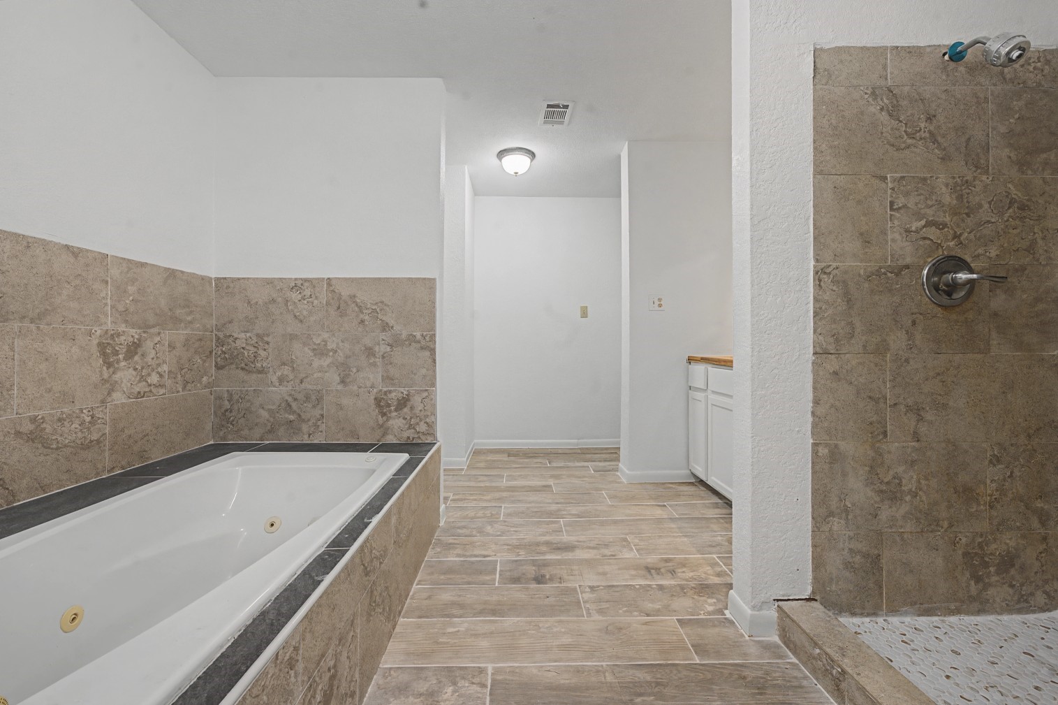 14077 Hamshire Road Hamshire, TX 77622 - Photo 21 of 39 This spacious bathroom features a luxurious soaking jacuzzi tub and a separate walk-in shower, both accented with elegant stone tiles. The room has a clean, modern aesthetic with ample natural light and a functional layout, ideal for relaxation and comfort.