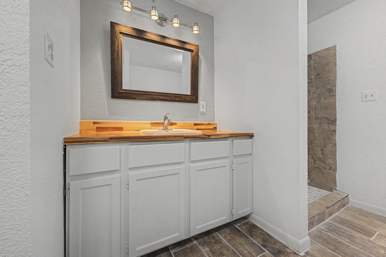 14077 Hamshire Road Hamshire, TX 77622 - Photo 22 of 39 This bathroom features a modern vanity with a wood countertop and a stylish mirror. It has white cabinetry, a sleek faucet, and overhead lighting. The adjacent area shows a tiled walk-in shower, adding to the contemporary feel.