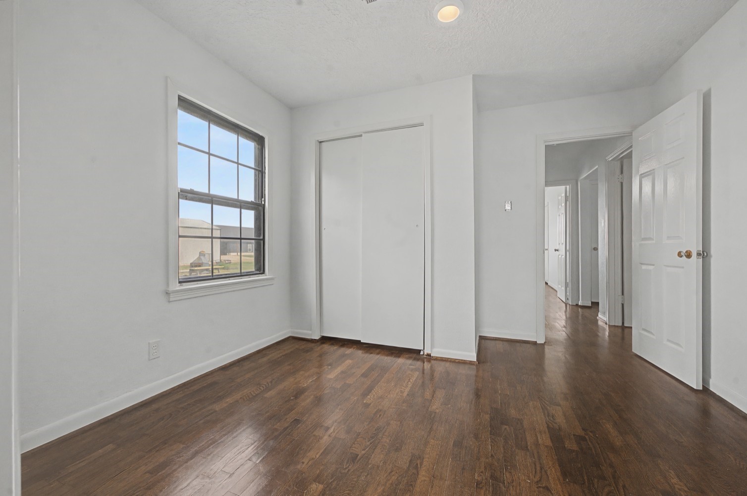 14077 Hamshire Road Hamshire, TX 77622 - Photo 25 of 39 This room features polished floors, neutral white walls, and a bright window offering natural light. It includes a closet and leads into a hallway with multiple doorways, perfect for a cozy bedroom or home office.