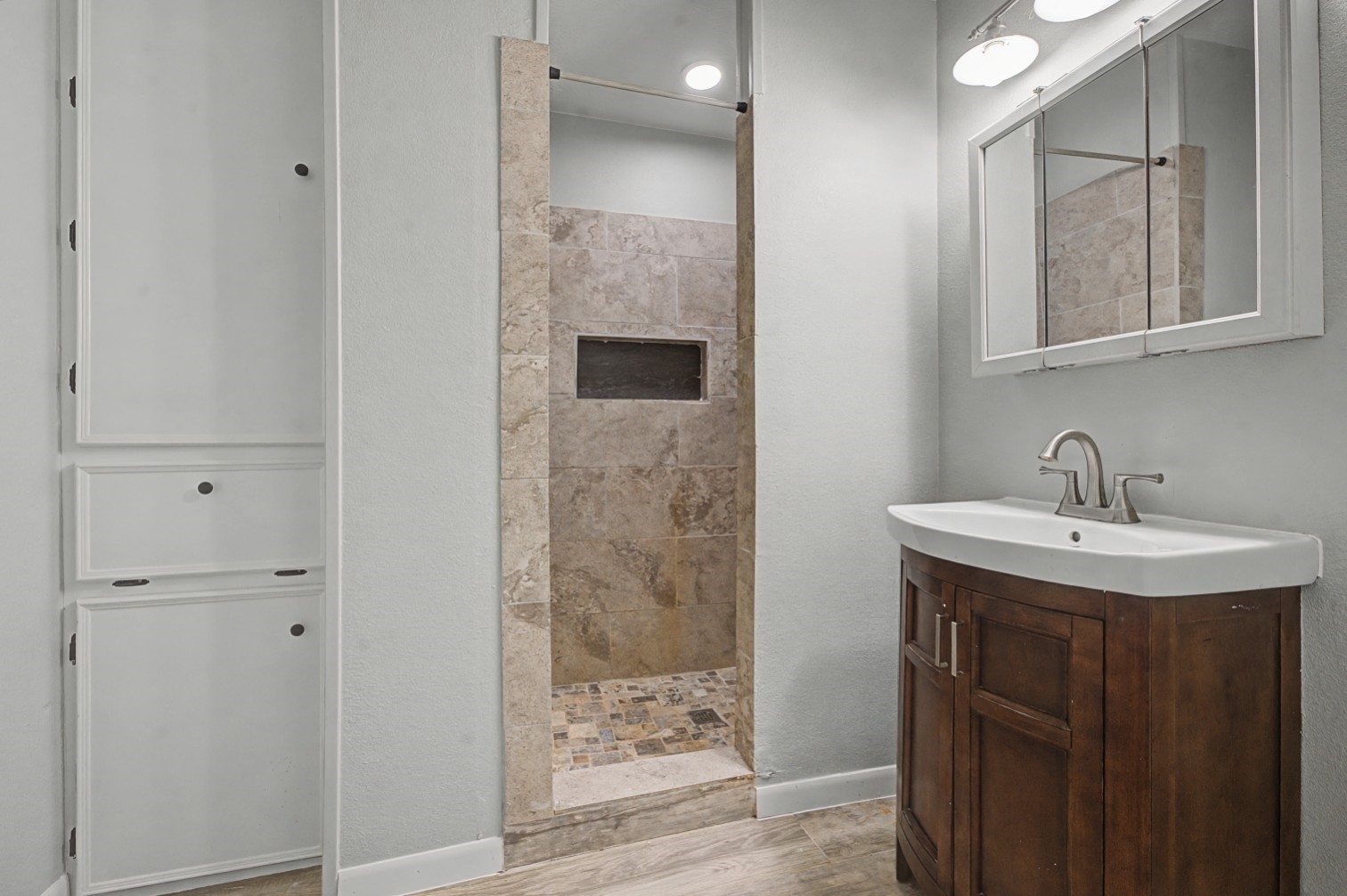 14077 Hamshire Road Hamshire, TX 77622 - Photo 26 of 39 This bathroom features a modern design with a sleek vanity and mirror, tiled walk-in shower, and built-in storage cabinets, offering both functionality and style.