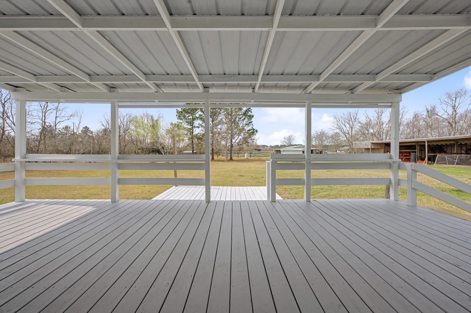 14077 Hamshire Road Hamshire, TX 77622 - Photo 30 of 39 This photo showcases a spacious covered deck with white railings, overlooking a large, open grassy yard with scattered trees, perfect for outdoor relaxation and gatherings.