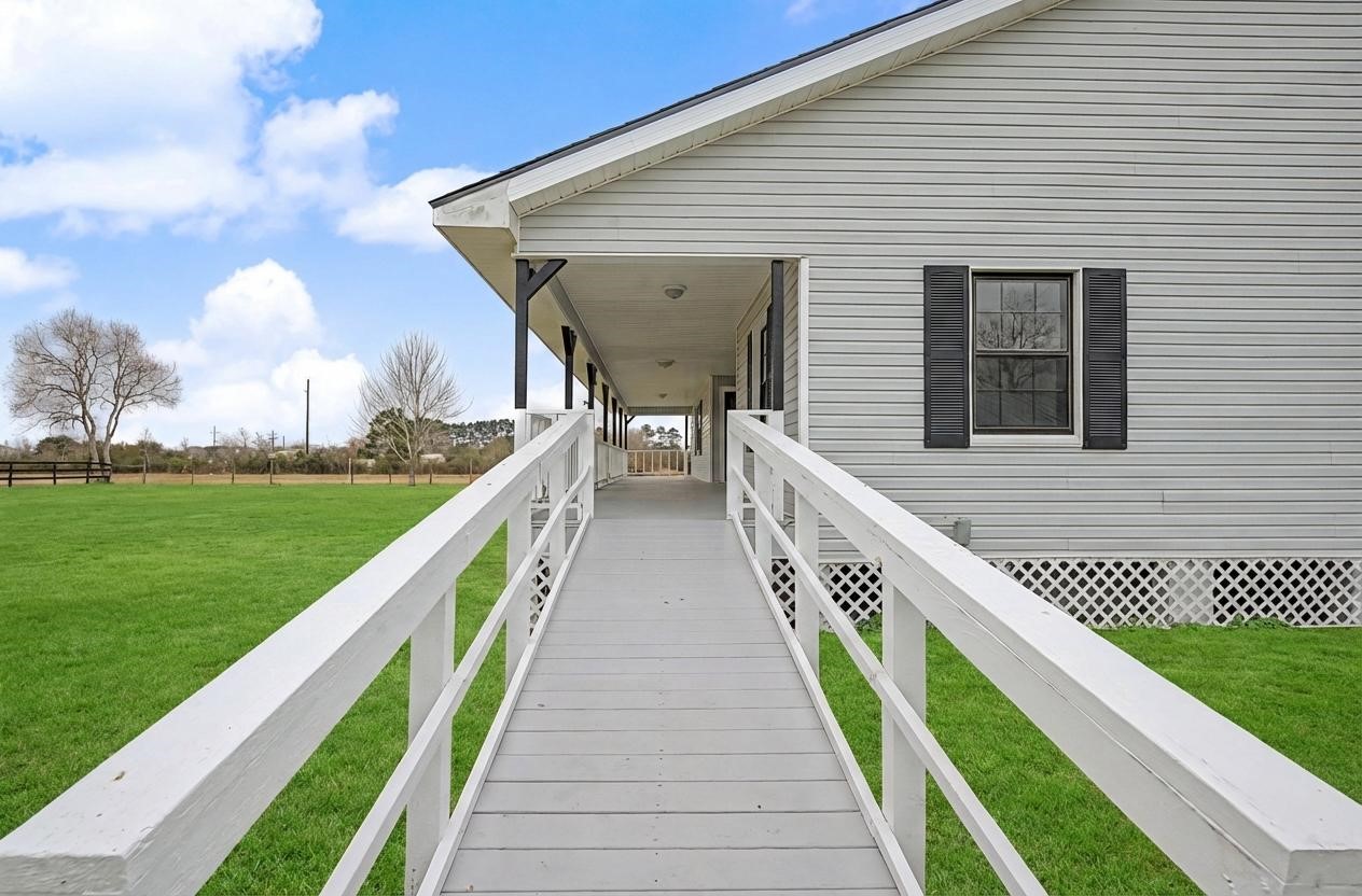 14077 Hamshire Road Hamshire, TX 77622 - Photo 3 of 39 This photo showcases a charming home with a welcoming front porch and a ramp for easy access. The exterior is light-colored with contrasting dark shutters. It sits on a spacious, well-maintained green lawn, perfect for outdoor activities.