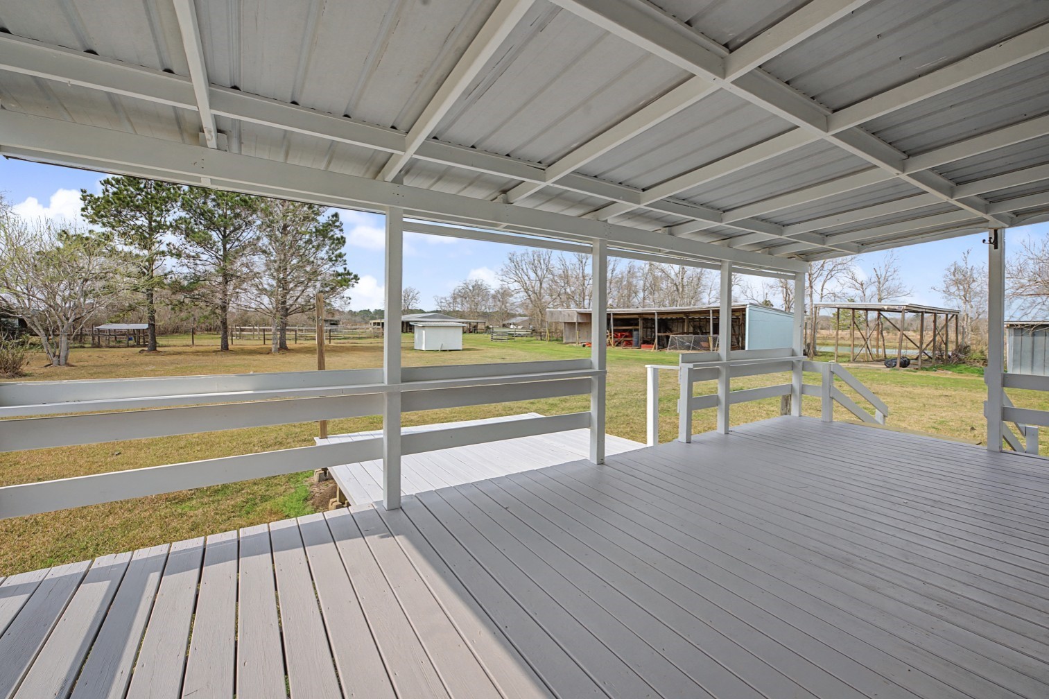 14077 Hamshire Road Hamshire, TX 77622 - Photo 31 of 39 This photo showcases a spacious covered deck overlooking a large backyard with trees and shed with 3 large stalls for animals or equipment.