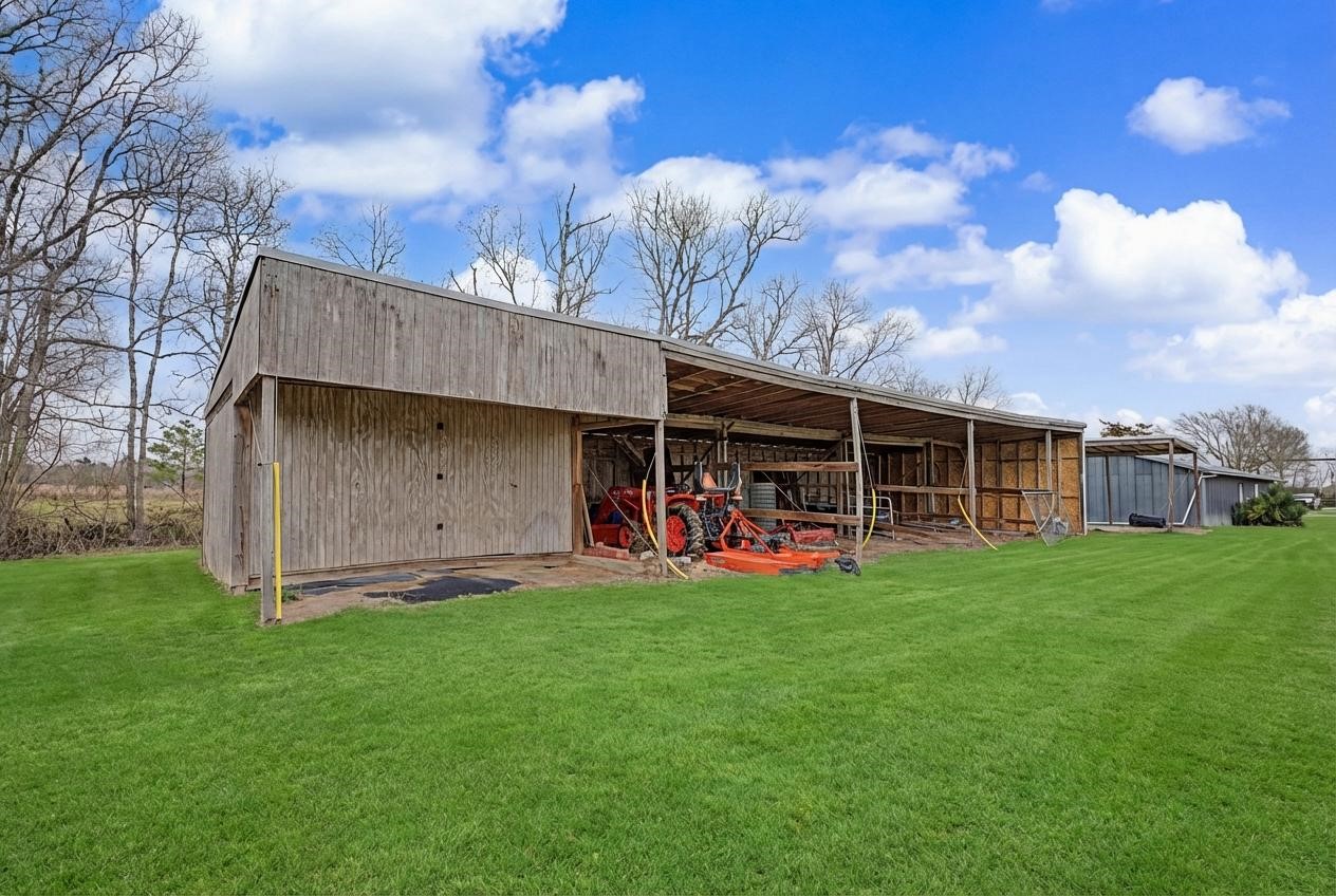14077 Hamshire Road Hamshire, TX 77622 - Photo 32 of 39 This photo shows a spacious wooden shed on a well-maintained grassy lot. It's surrounded by a few trees and set under a clear blue sky.