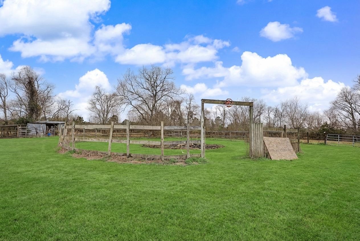 14077 Hamshire Road Hamshire, TX 77622 - Photo 35 of 39 This photo shows a spacious, grassy yard with a round fenced area, ideal for outdoor activities. The sky is clear with scattered clouds, and there are mature trees in the background, offering a serene rural setting.