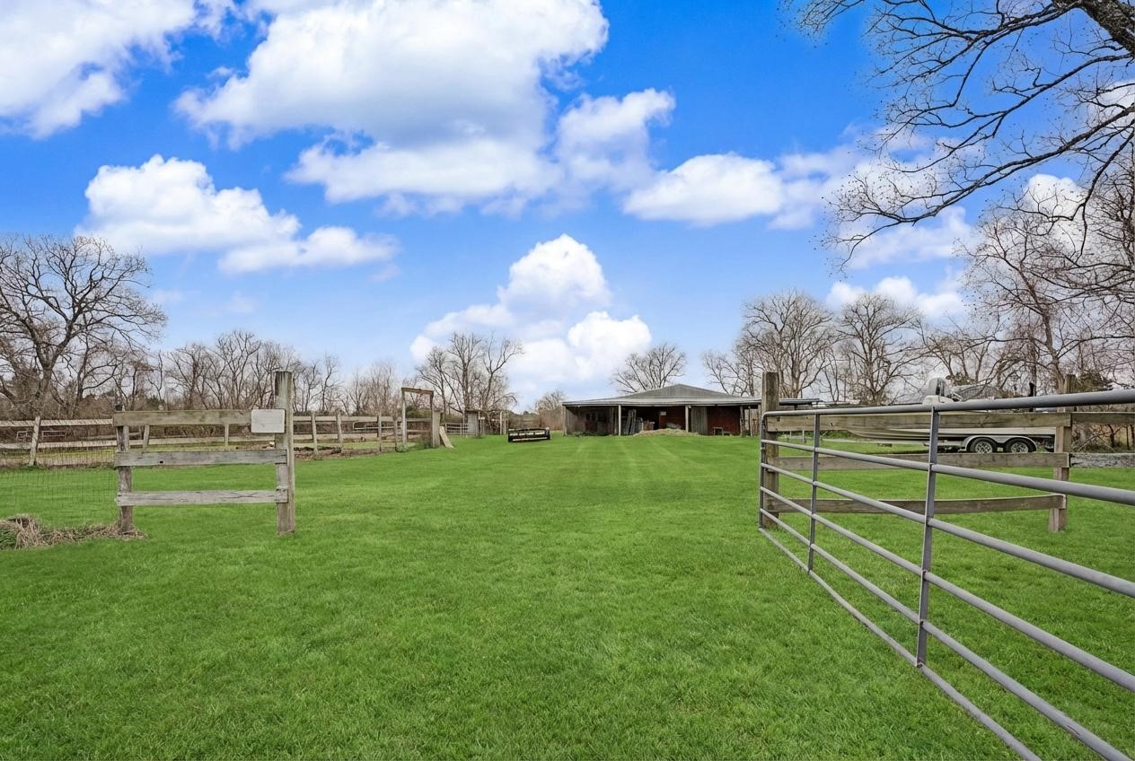 14077 Hamshire Road Hamshire, TX 77622 - Photo 36 of 39 Expansive property with lush green lawn and rustic fencing, featuring a spacious arenas and stables in the distance. Ideal for those seeking a serene, rural setting.