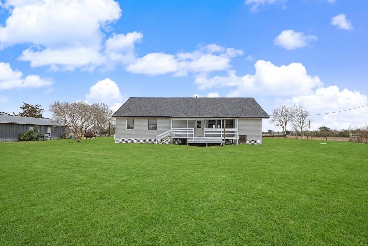 14077 Hamshire Road Hamshire, TX 77622 - Photo 39 of 39 This photo features a single-story home with a white exterior, surrounded by a large, well-maintained grassy yard. The house has porch with steps leading to a spacious open area. It's set in a rural location with clear skies adding to the serene environment.