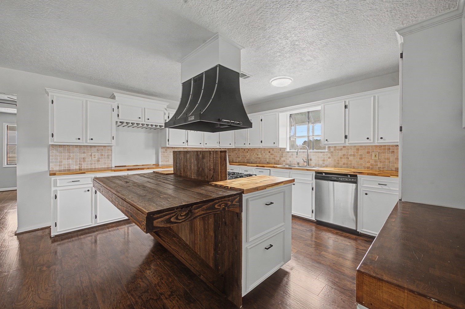 14077 Hamshire Road Hamshire, TX 77622 - Photo 7 of 39 This kitchen features a rustic wooden island with a unique design, complemented by white cabinetry and a modern range hood. It includes stainless steel appliances and a warm tile backsplash, creating a cozy yet contemporary feel.