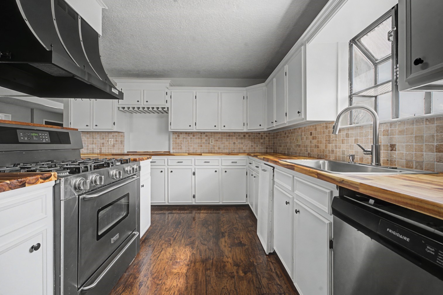 14077 Hamshire Road Hamshire, TX 77622 - Photo 8 of 39 This kitchen features modern stainless steel appliances, white cabinetry, wood countertops, and a tiled backsplash. The dark wood flooring complements the bright, open layout, creating a warm and inviting space.