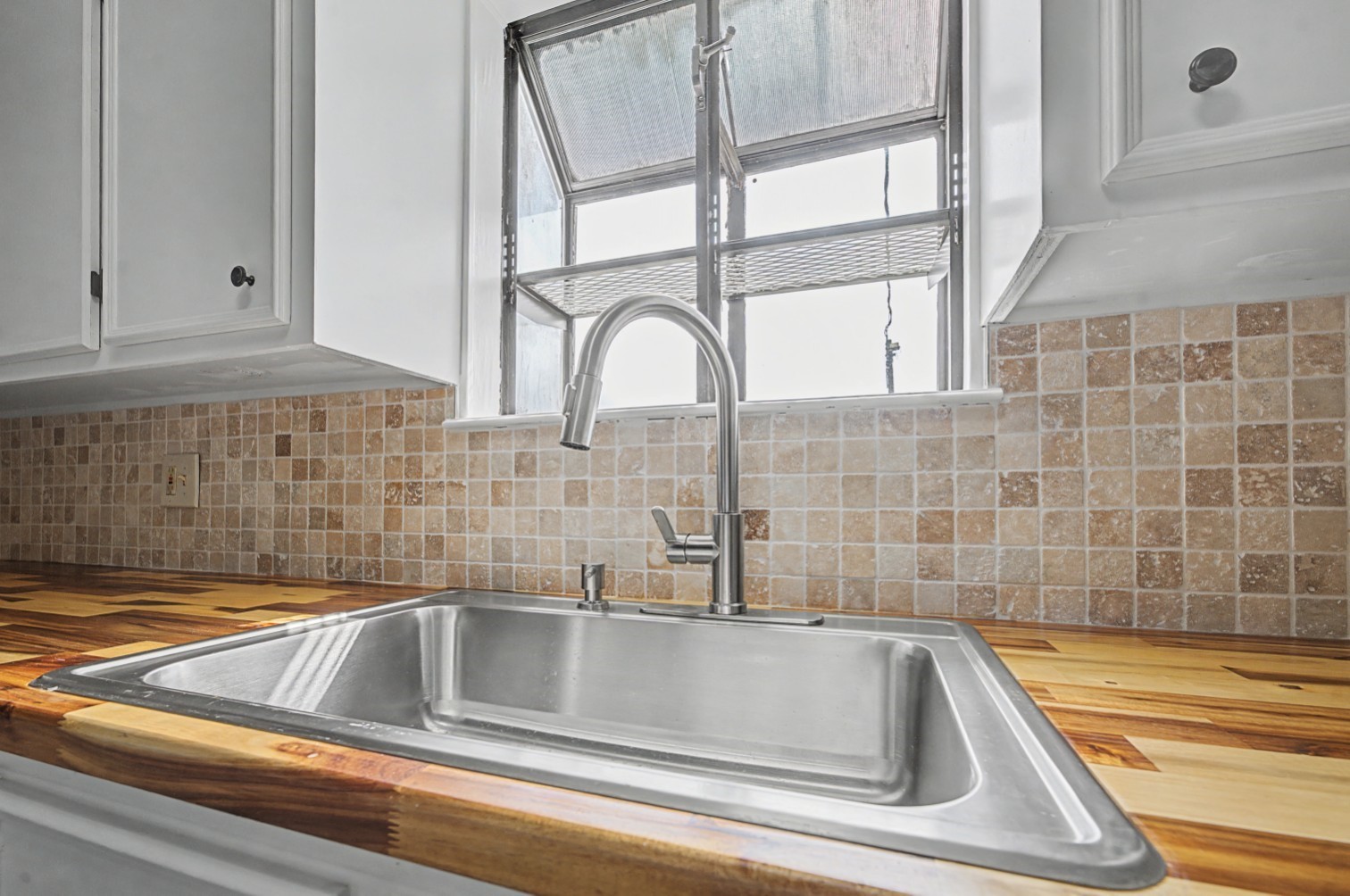 14077 Hamshire Road Hamshire, TX 77622 - Photo 9 of 39 This kitchen features a sleek stainless steel sink with a modern faucet, set against a warm wood butcher block countertop and textured tile backsplash, offering a blend of style and functionality.